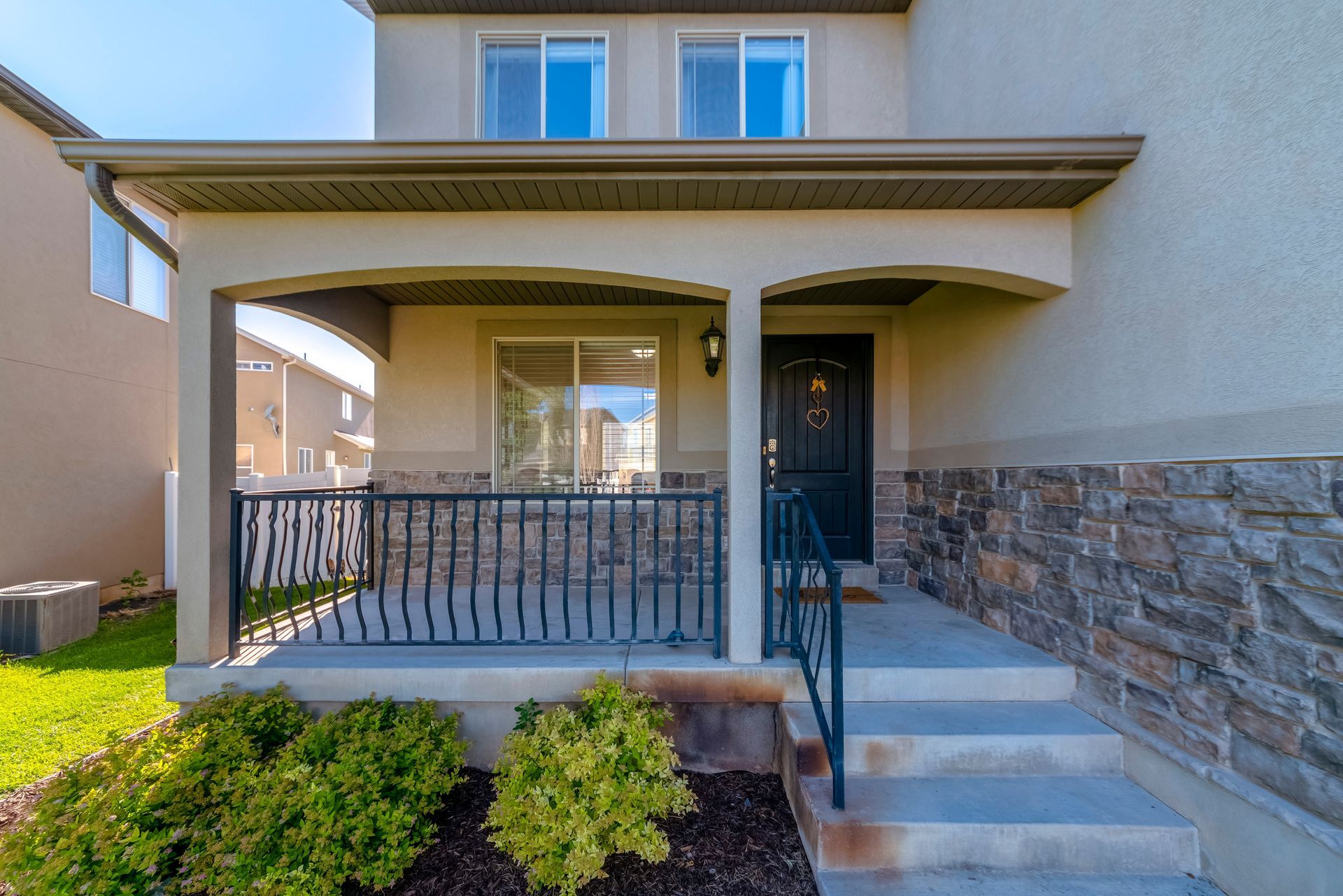 Beige and stone facade home with covered porch, front door, and small front yard with bushes.