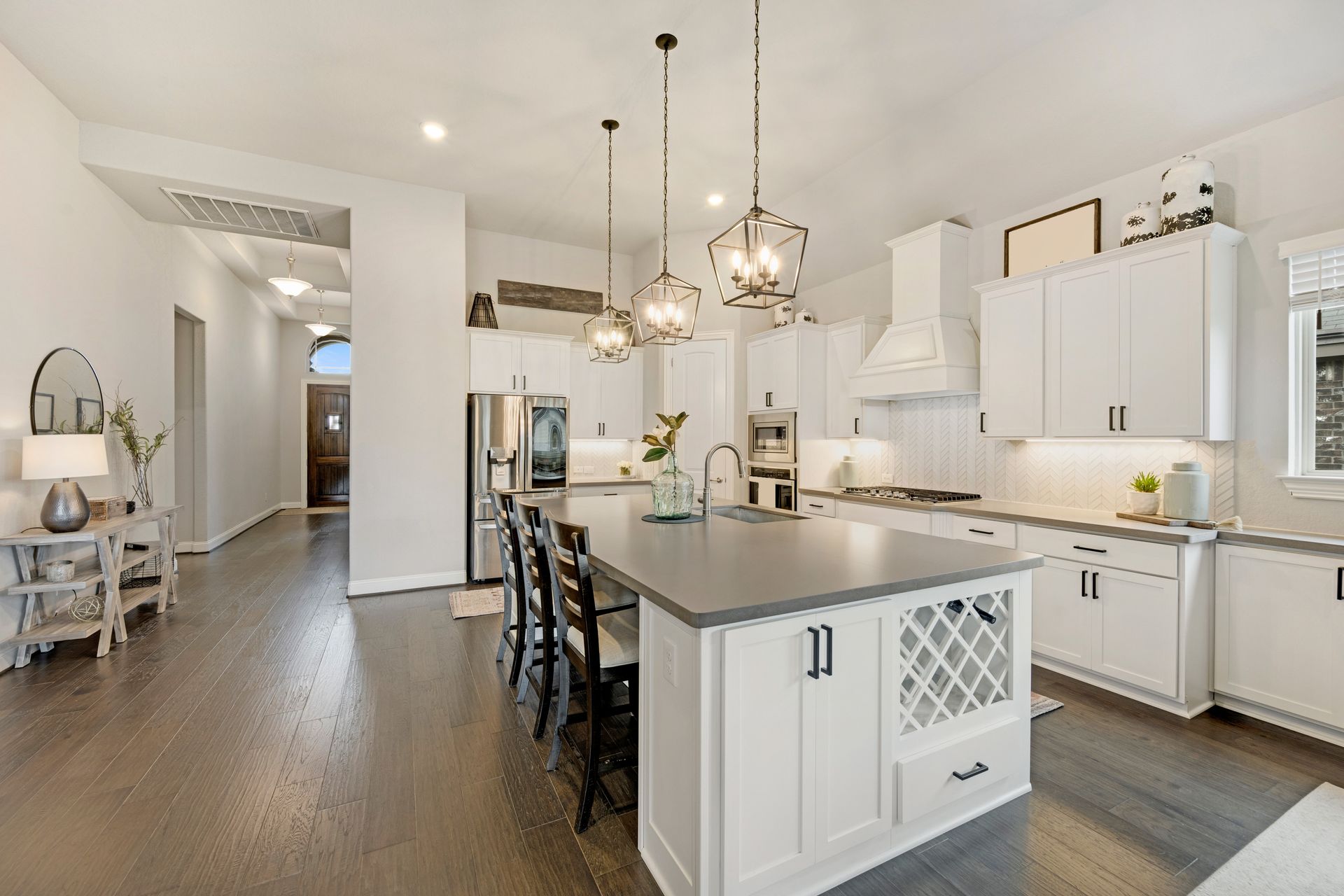 Spacious white kitchen with island, pendant lights, and dark wood floors.