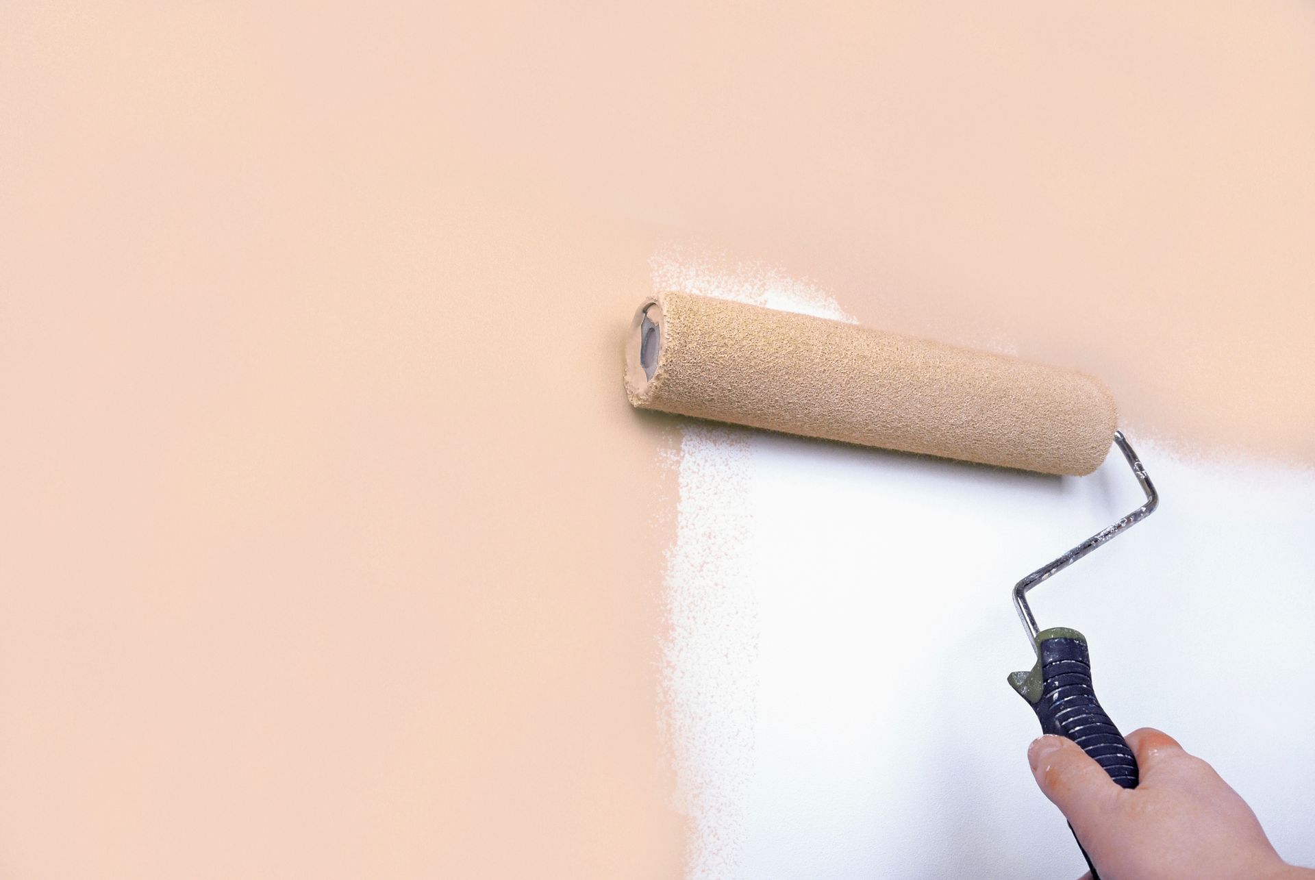 Hand painting a wall with a paint roller, covering peach with white.