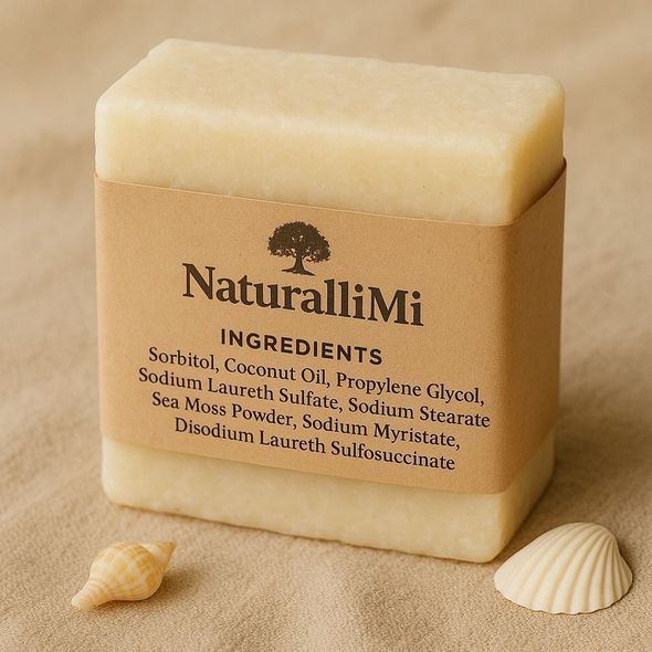 A bar of soap with a NaturalliMi label sits on sand, next to a seashell. Soap ingredients are listed.