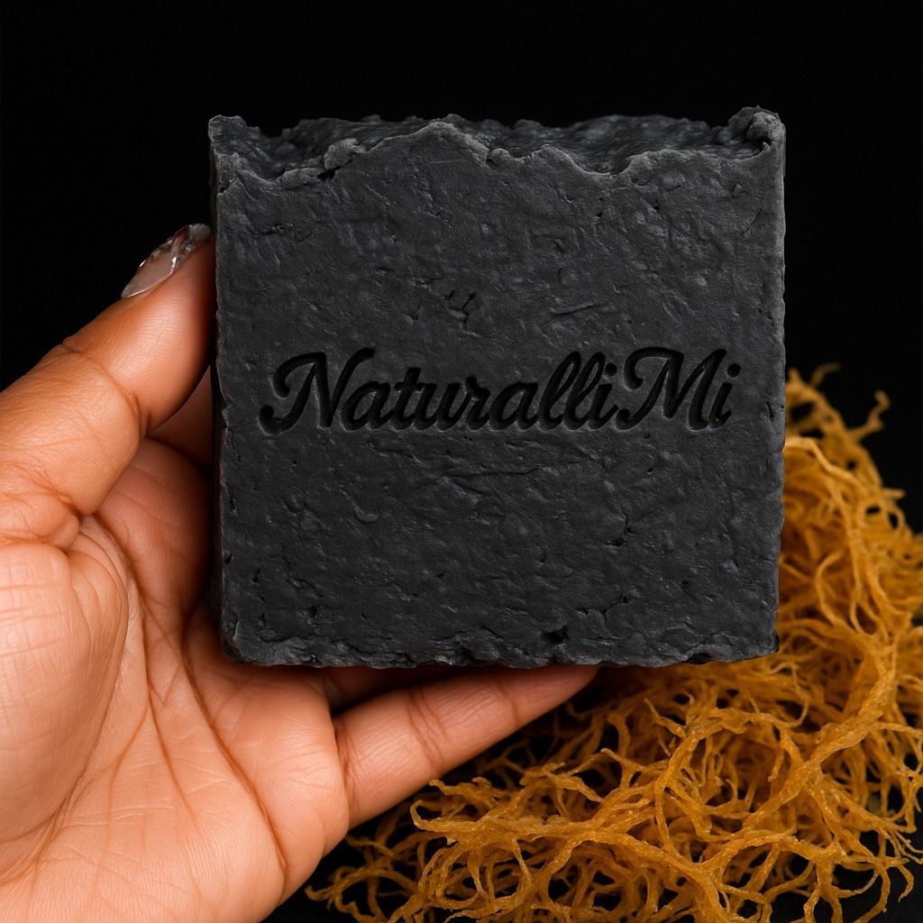 A black soap bar with the words "Naturalii Mi" held by a person's hand, beside sea moss.