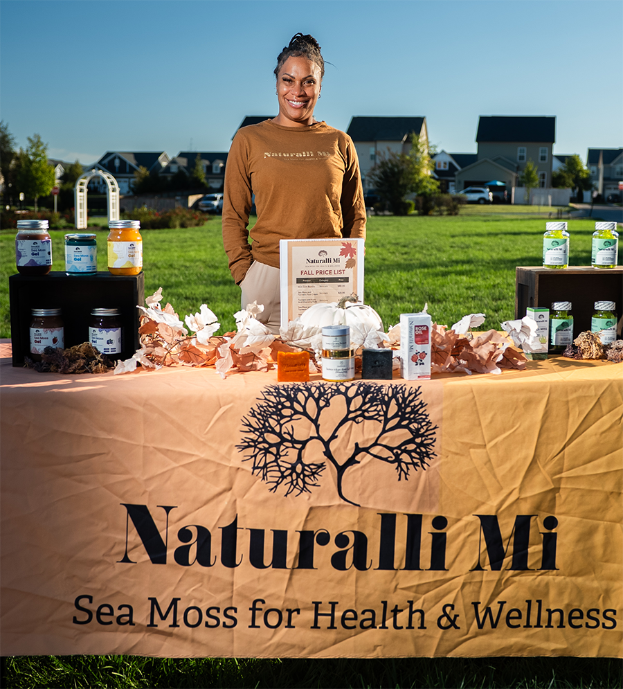 Woman at outdoor market stand for Naturalli Mi sea moss products. Sunny day.