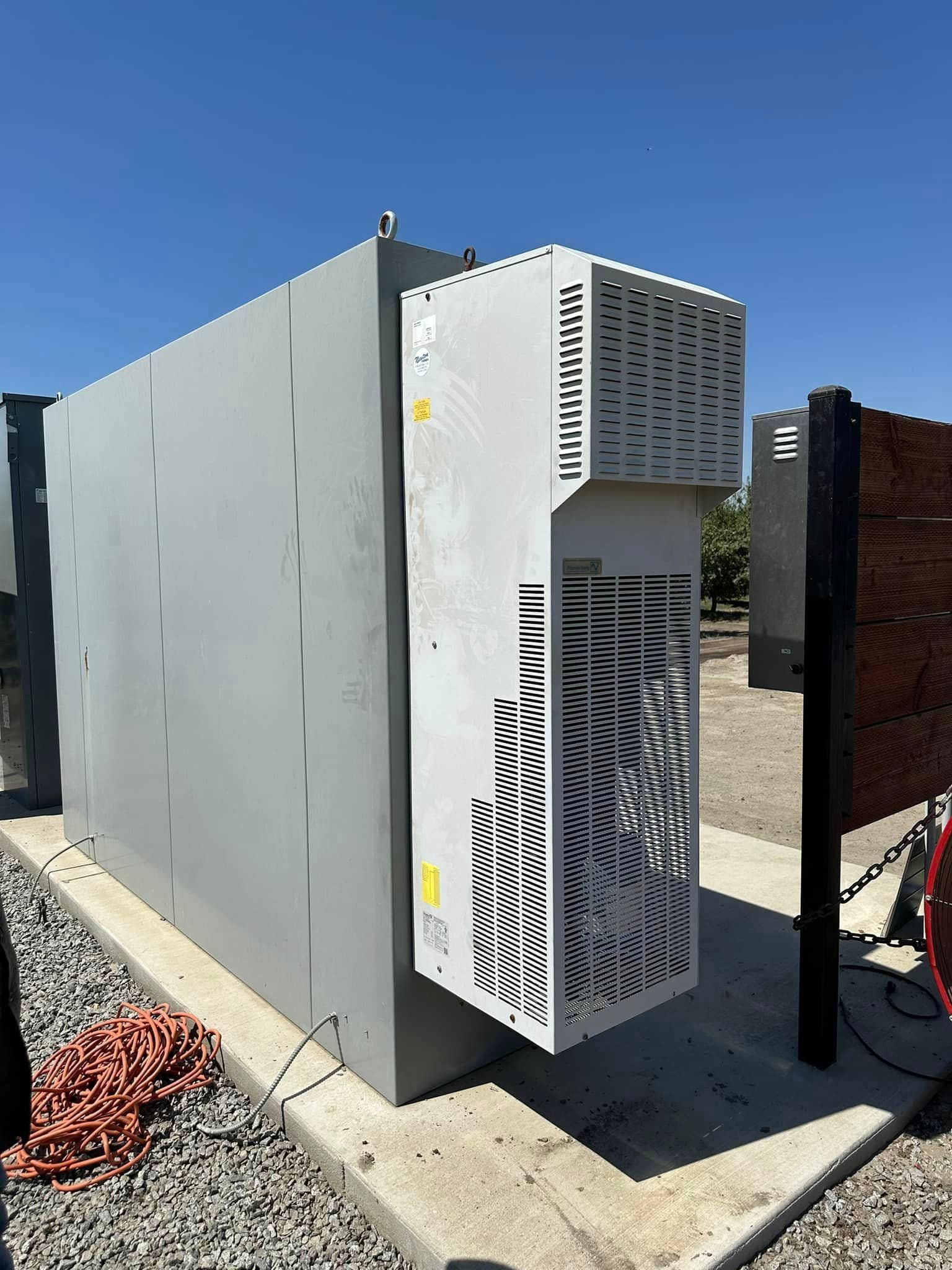 Large, grey industrial unit with ventilation grates, outdoors on a sunny day.