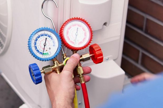 Hand using gauges connected to an air conditioning unit, checking pressure; two colored pressure gauges.