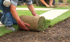 A man is rolling a roll of grass on the ground.