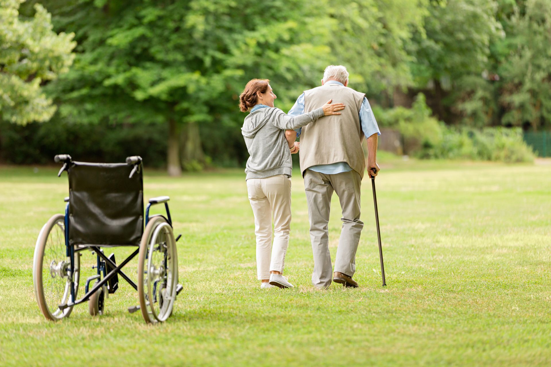 Caregiver assisting an elderly Black woman, seated on a couch, using a walker in a living room.