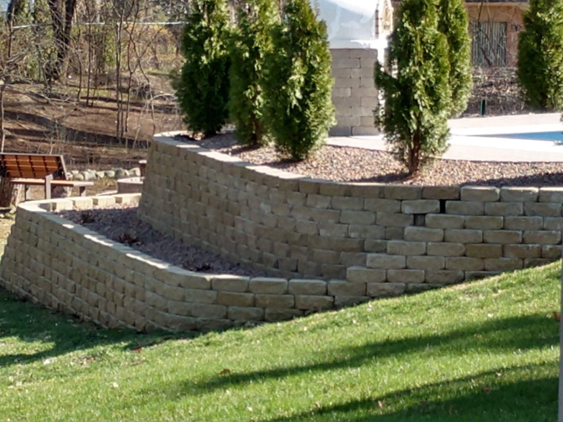 Garden with tall bushes and a retainer wall made of grey bricks  
