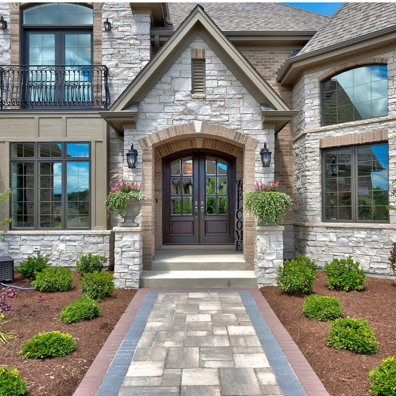 Stone house exterior with double doors, arched entryway, and landscaped front yard.