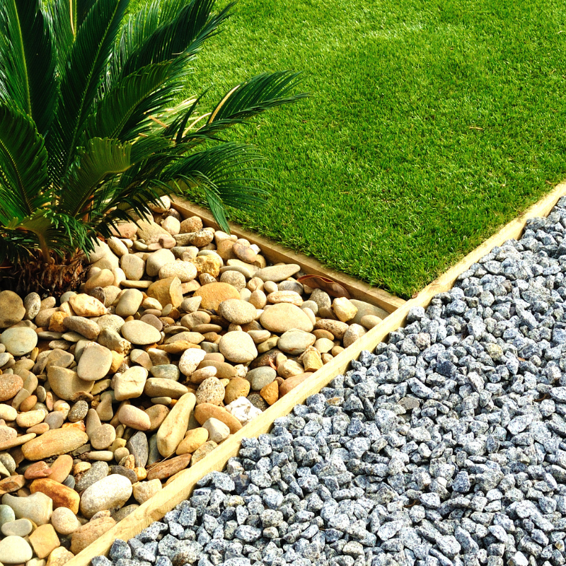 Bordered garden bed with rocks, grass, and a palm plant.