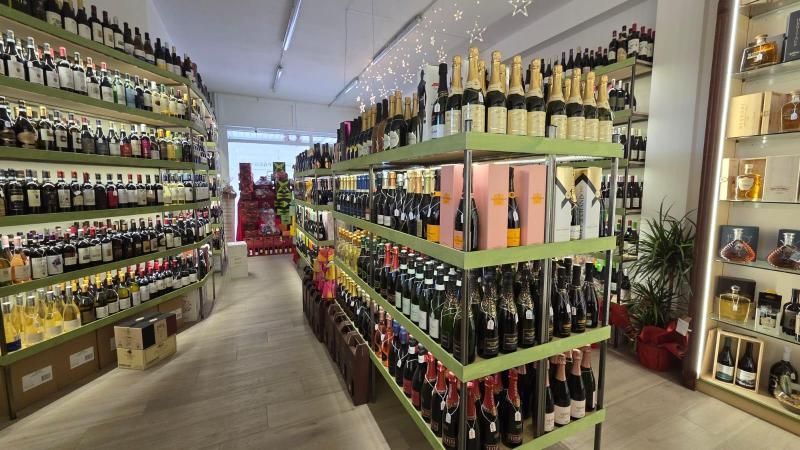 Vista interna di un negozio di liquori con varie bottiglie di vino e altre bevande alcoliche esposte sugli scaffali.