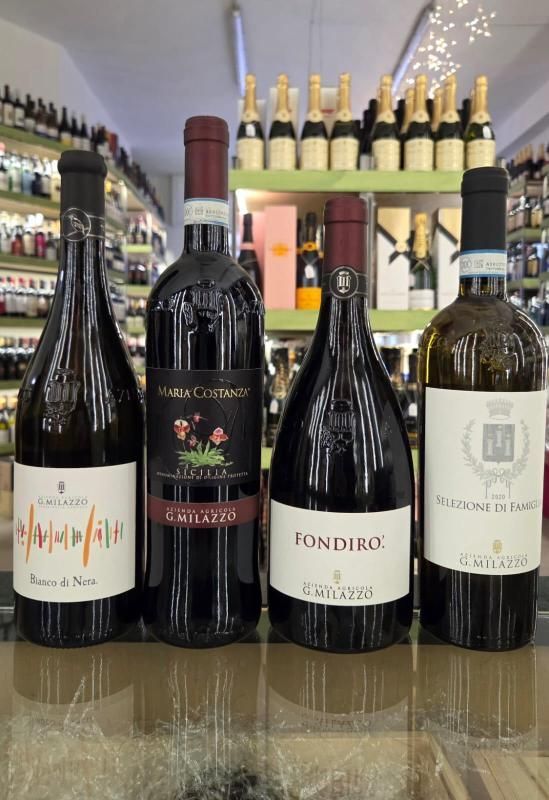 Quattro bottiglie di vino, di varie forme ed etichette, esposte su un bancone con altre bottiglie di vino sullo sfondo.