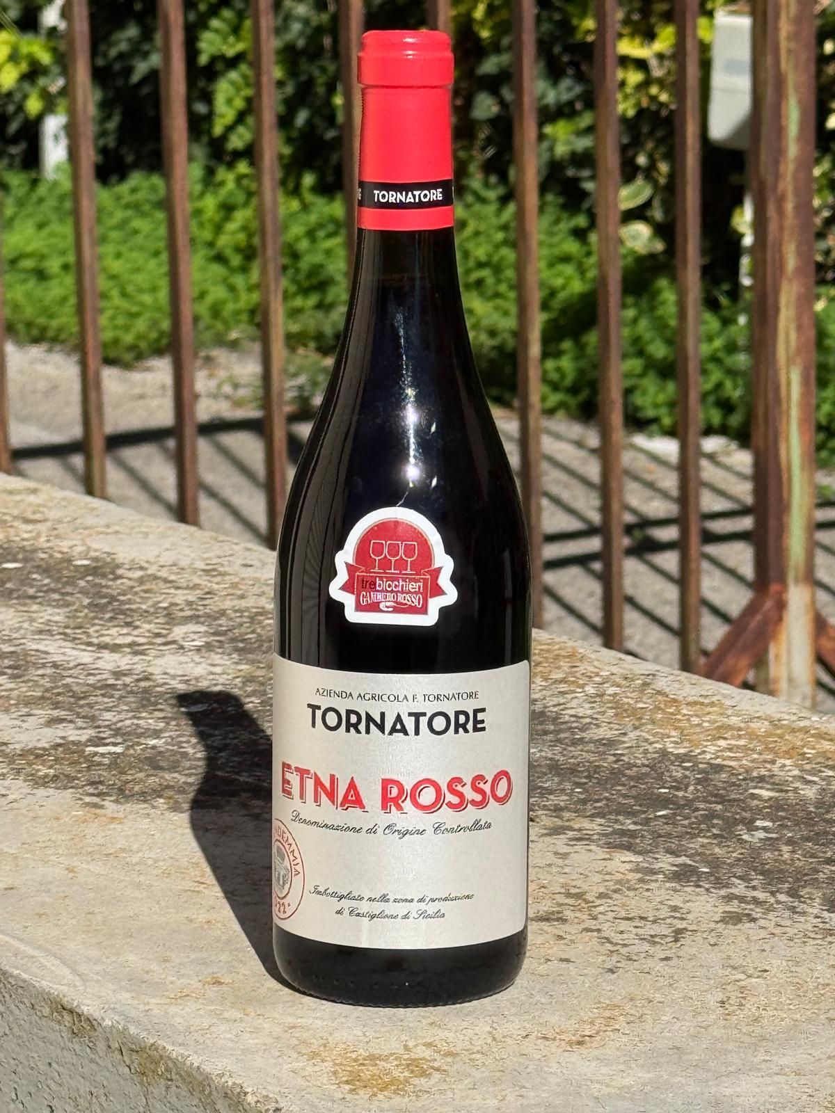 Bottiglia di vino Tornatore Etna Rosso con tappo rosso, etichetta e sfondo di mattoni.