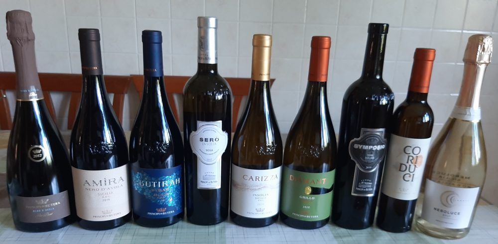 Nove bottiglie di vino appoggiate su una superficie, con colori ed etichette diversi.