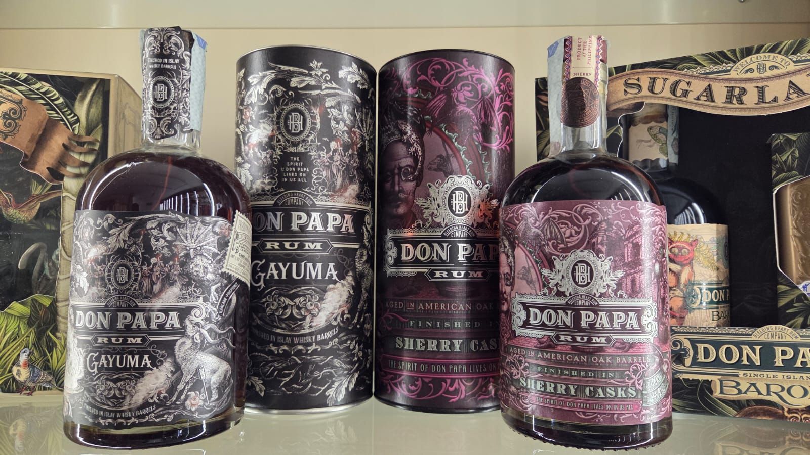 Quattro bottiglie e contenitori di rum Don Papa su uno scaffale con etichette decorative, in un ambiente buio.