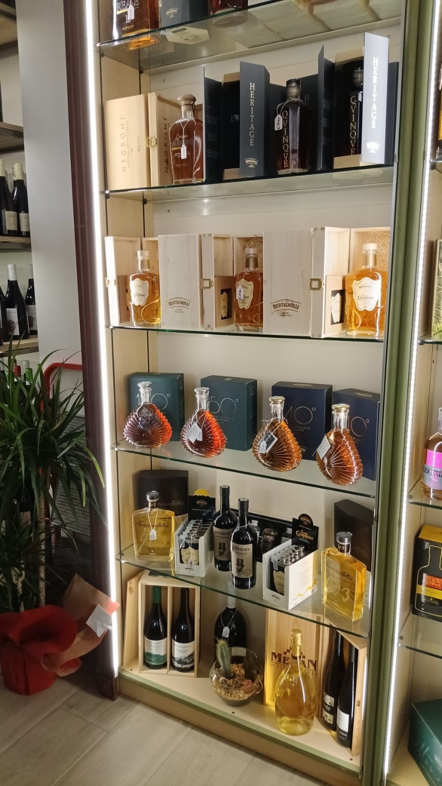 Vetrina in vetro piena di bottiglie di liquore di vario tipo, illuminata da luci verticali.