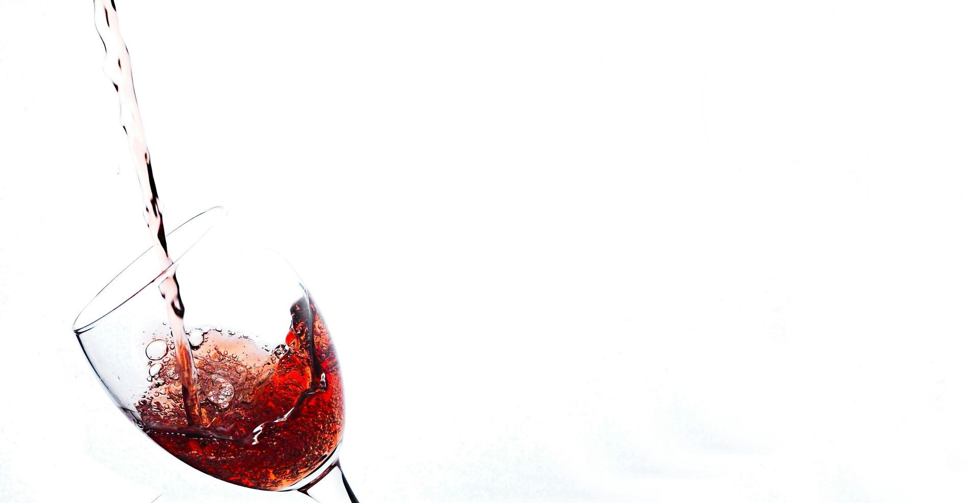 Liquido rosso versato in un bicchiere da vino su uno sfondo bianco.