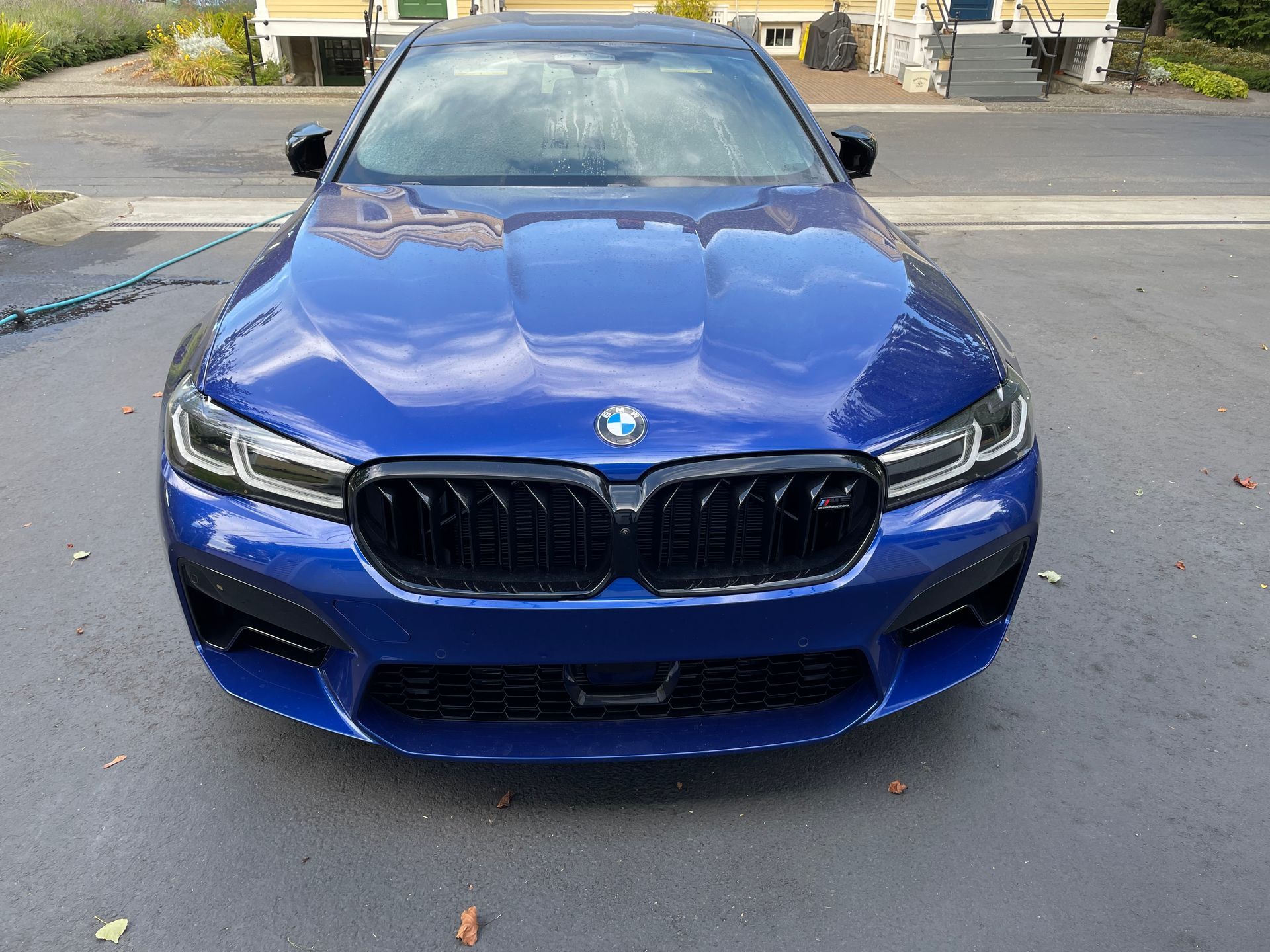 Blue BMW car parked on a driveway, front view. Black grill, black mirrors, and bright headlights.
