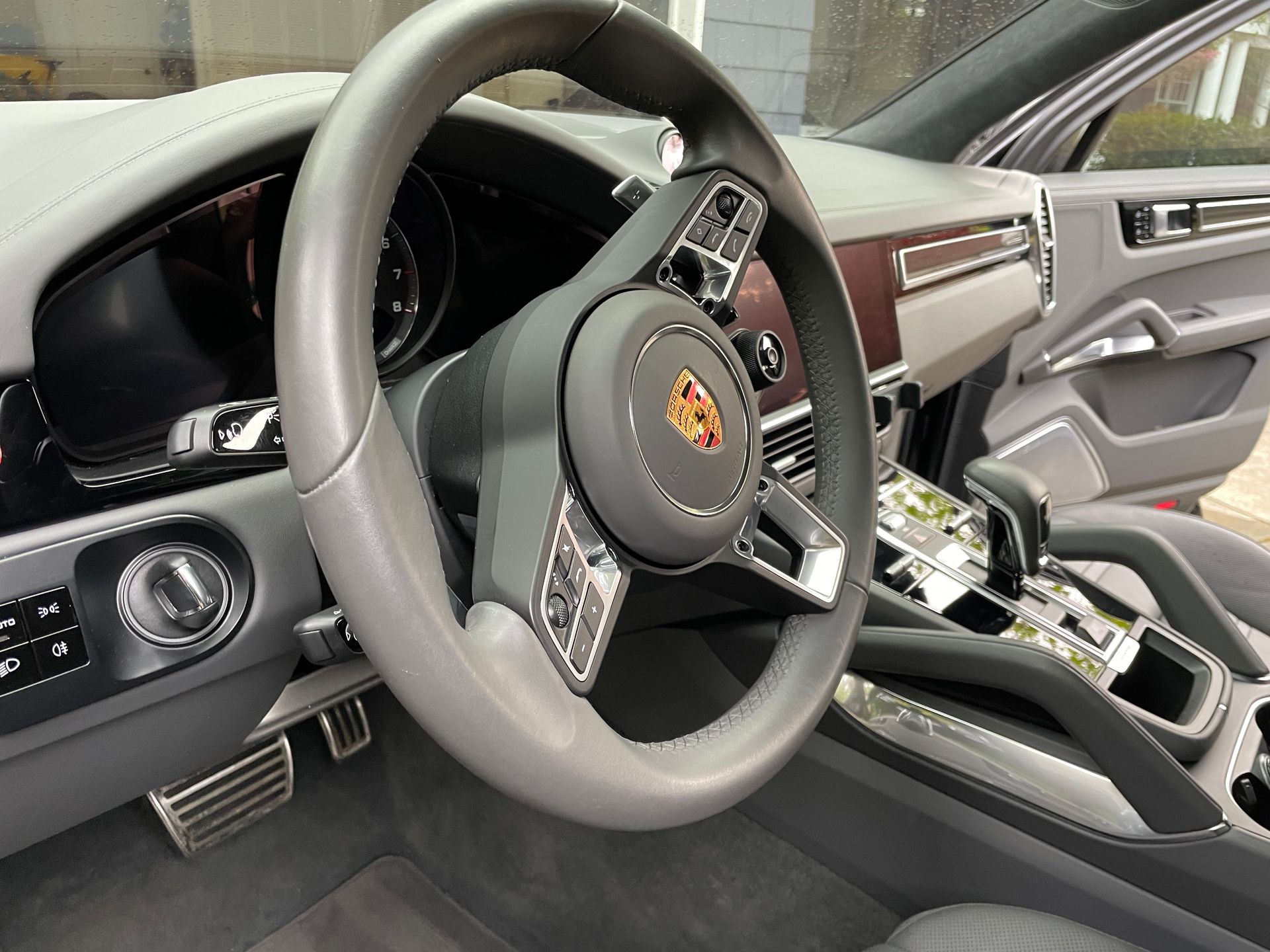Interior view of a Porsche Cayenne car dashboard, steering wheel, and console in gray, black, and wood.