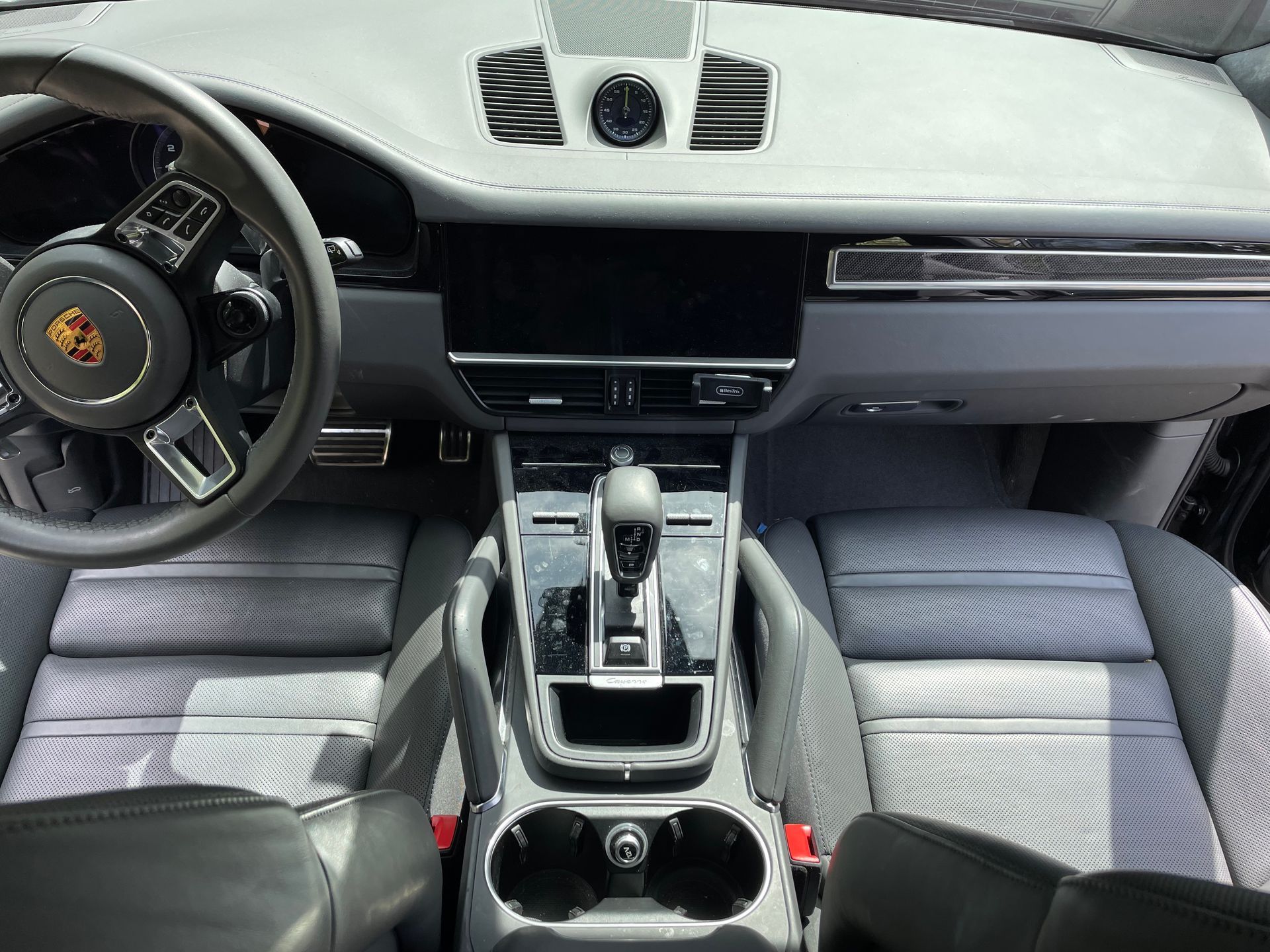 Interior of a gray Porsche SUV, showing the dashboard, seats, steering wheel, and gear shift.
