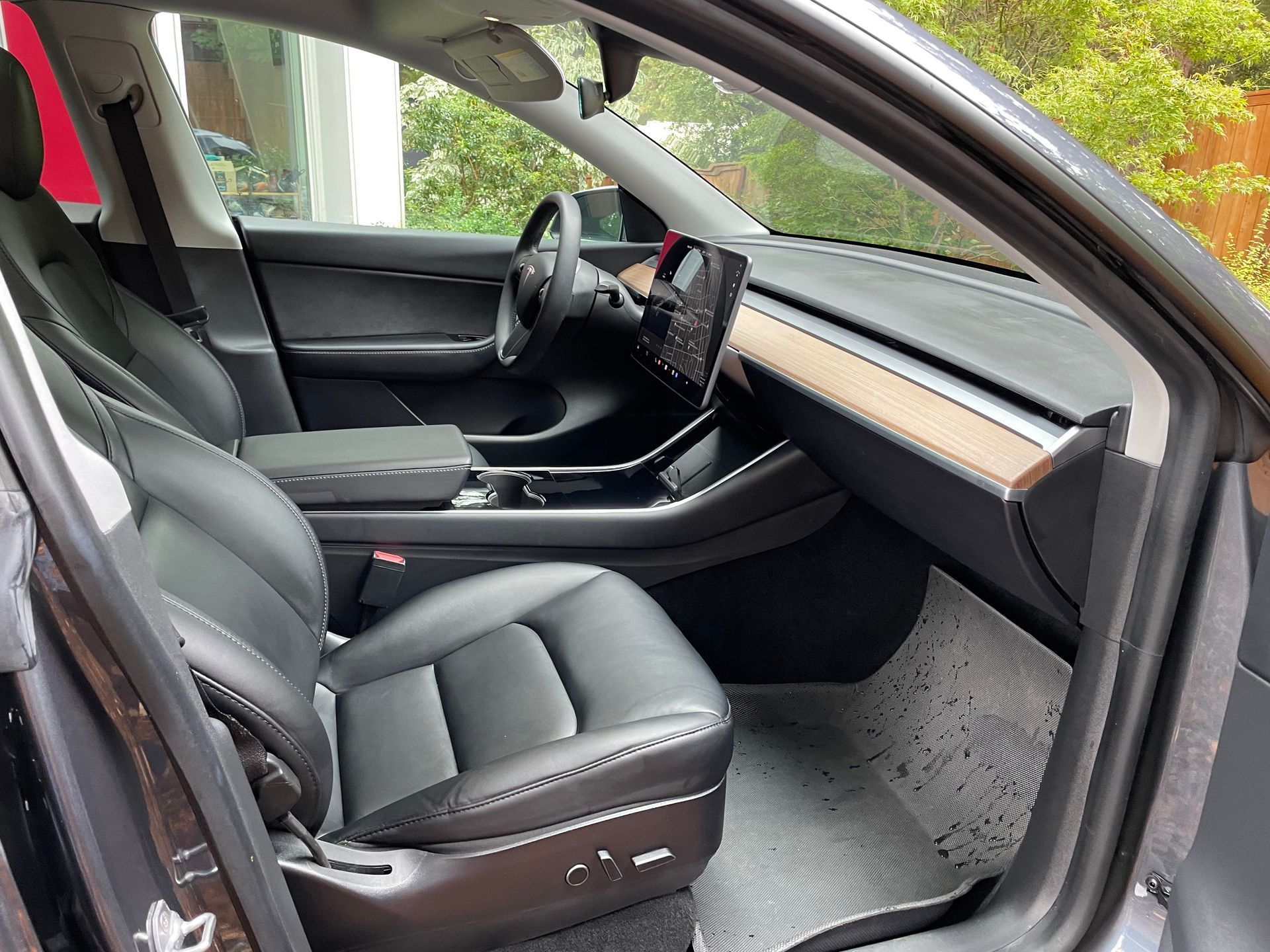 Black interior of a Tesla car: leather seats, dashboard, steering wheel, and floor mats are visible.