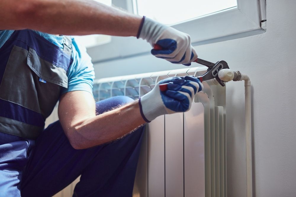 A Man is Fixing a Radiator With a Wrench — Gary Eslick Home Improvements In Berkeley Vale, NSW
