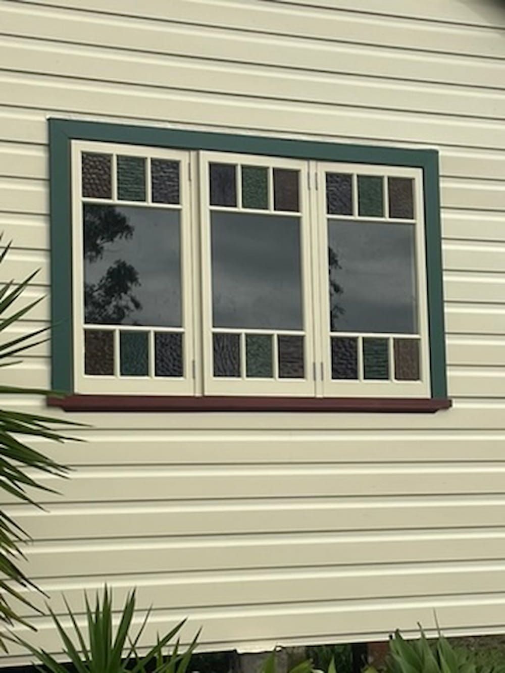 Window with stained-glass accents, green trim, and white siding. — Gary Eslick Home Improvements In Berkeley Vale, NSW