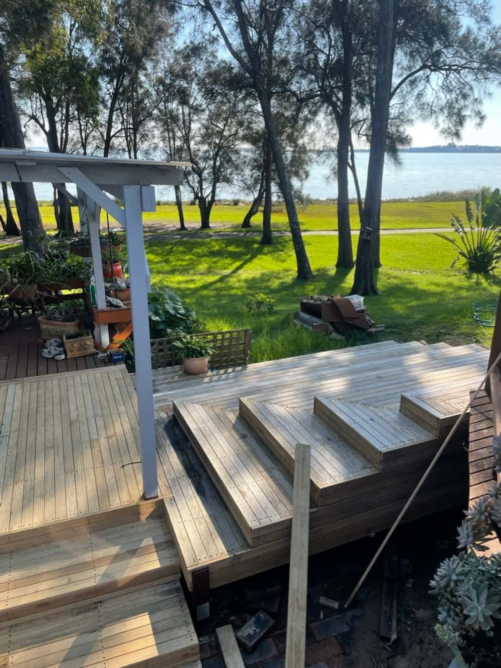 Wooden deck and steps leading to a green lawn with a water view and trees. — Gary Eslick Home Improvements In Berkeley Vale, NSW