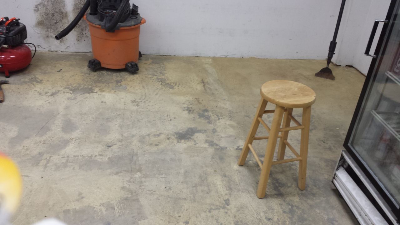 A wooden stool is sitting in a room next to a vacuum cleaner.