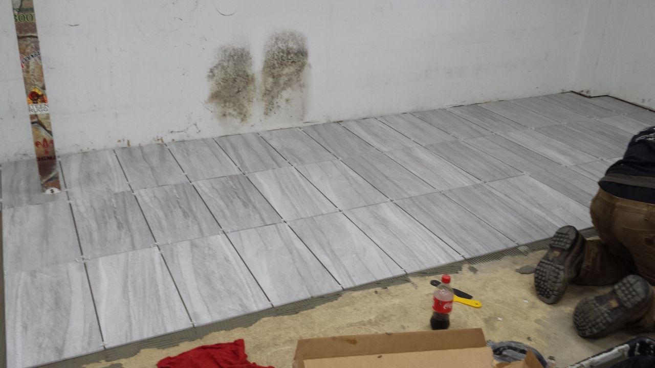A person is laying tiles on a floor in a room.