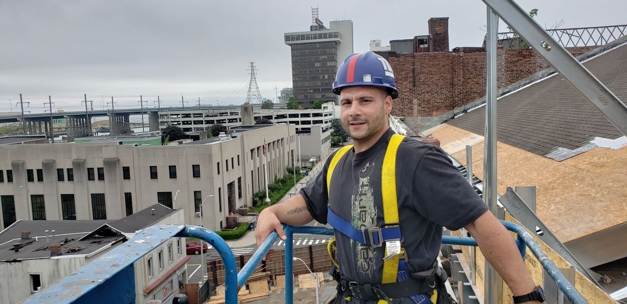 A man wearing a hard hat and safety harness is standing on top of a building.