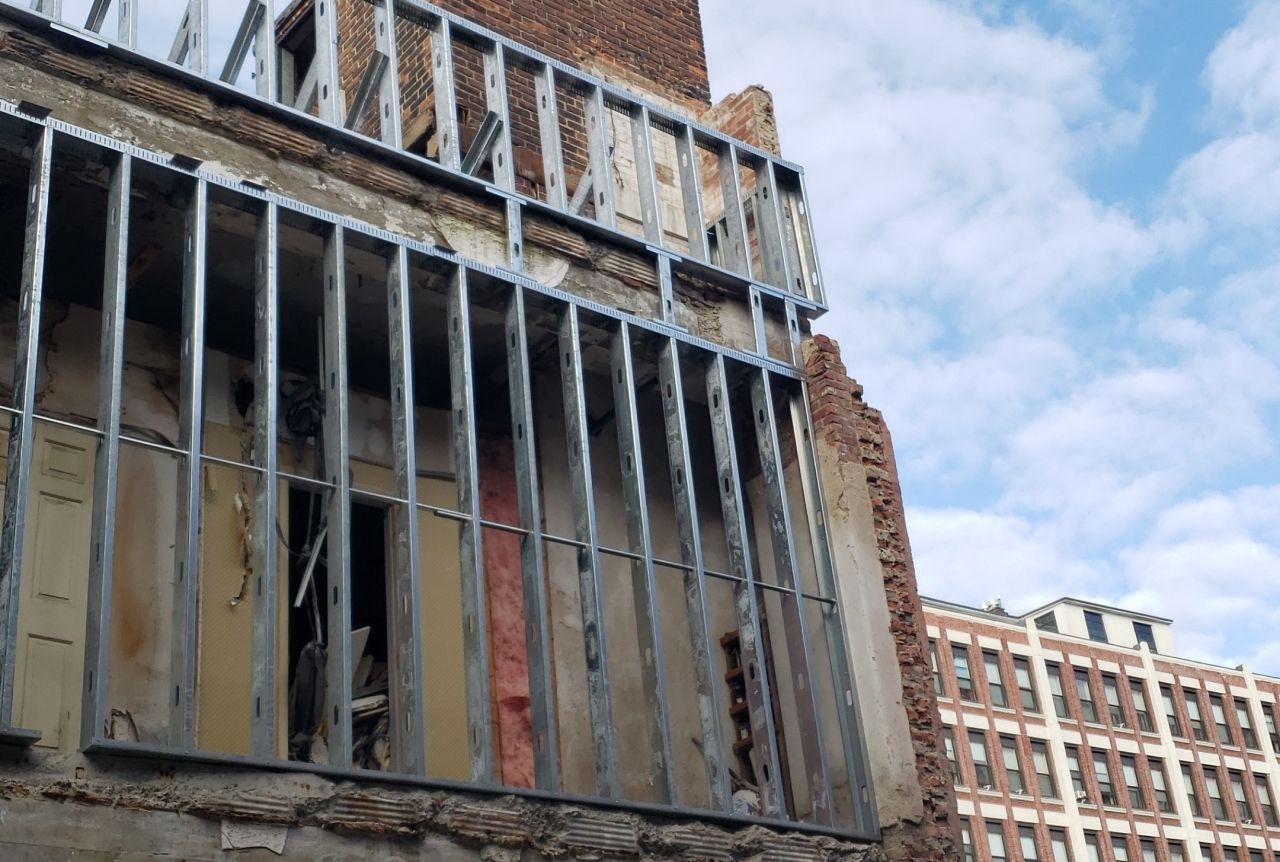 A building under construction with a brick building in the background.