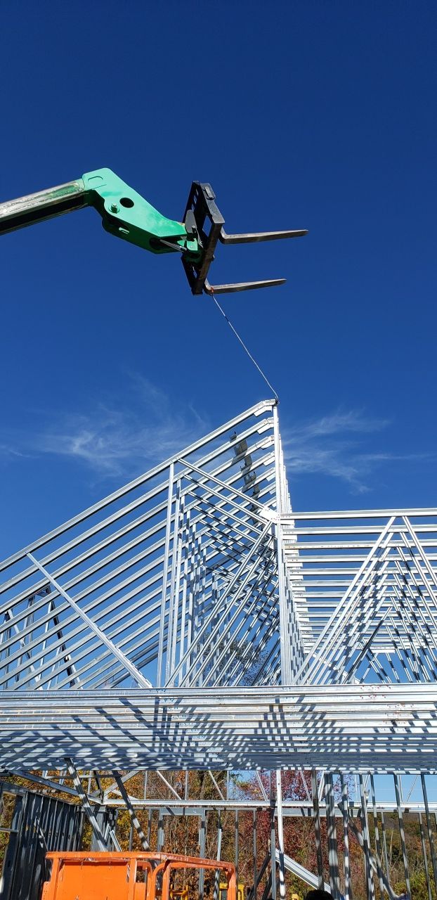 A forklift is lifting a metal structure on a construction site.
