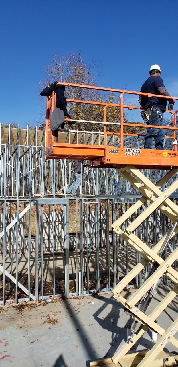 A man is standing on a scissor lift at a construction site.