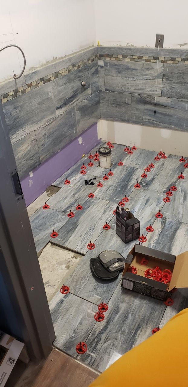 A bathroom is being remodeled with tile and a box of tile spacers on the floor.