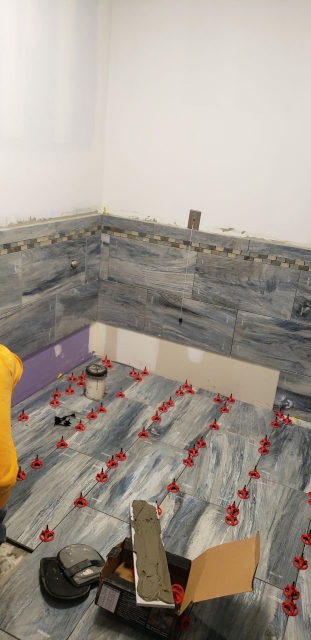 A person is laying tiles on the floor of a bathroom.