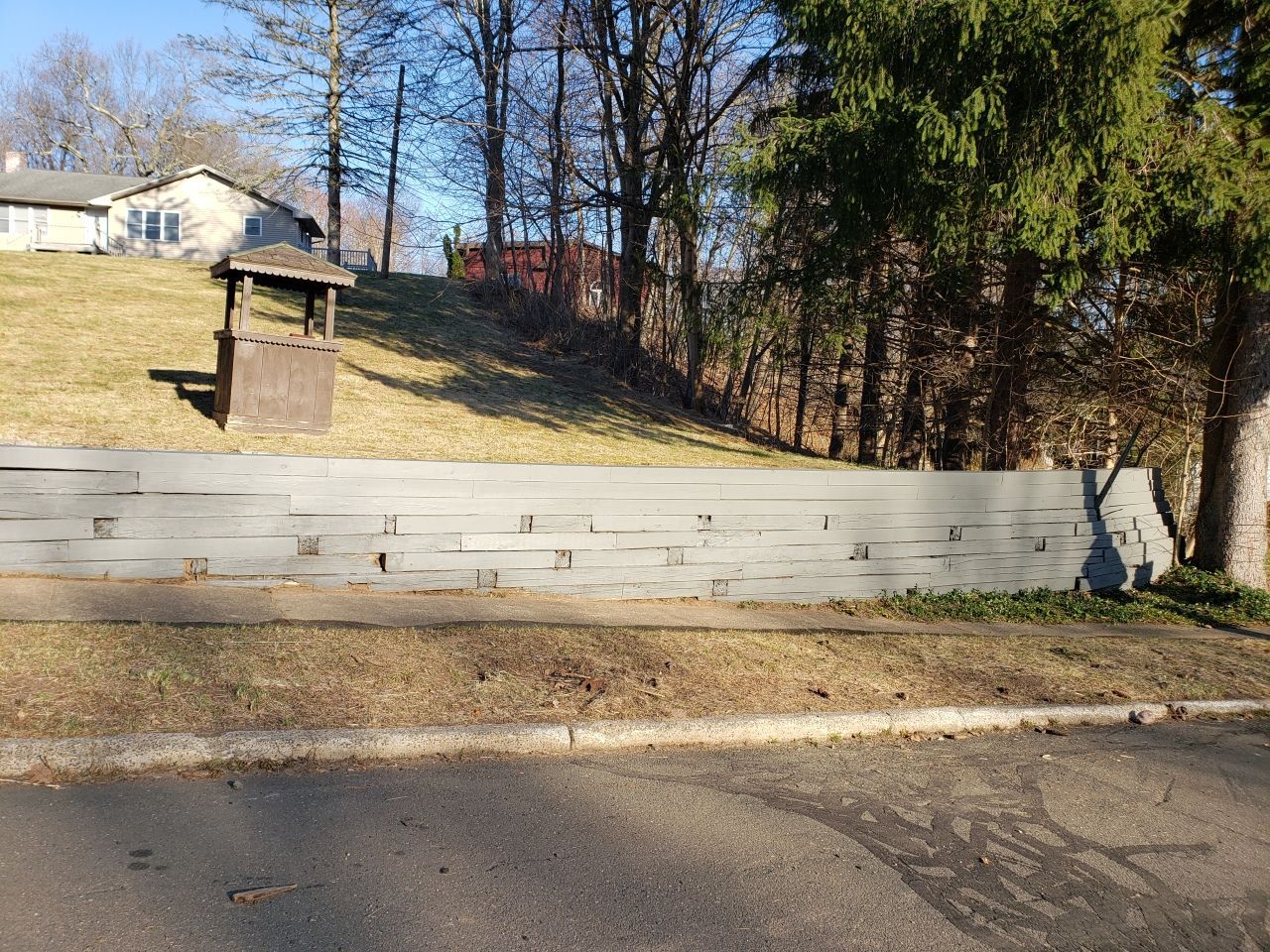 A wooden fence is sitting on the side of a road next to a house.