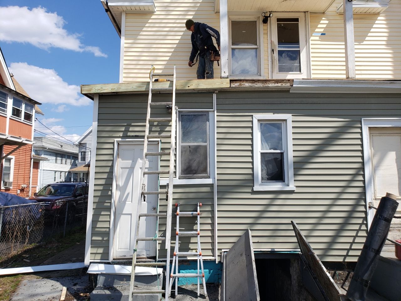 A man is standing on the roof of a house with a ladder.