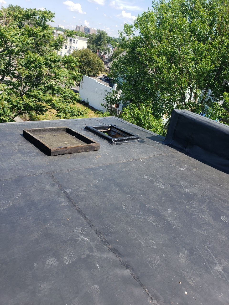 A black roof with a hole in it and trees in the background.