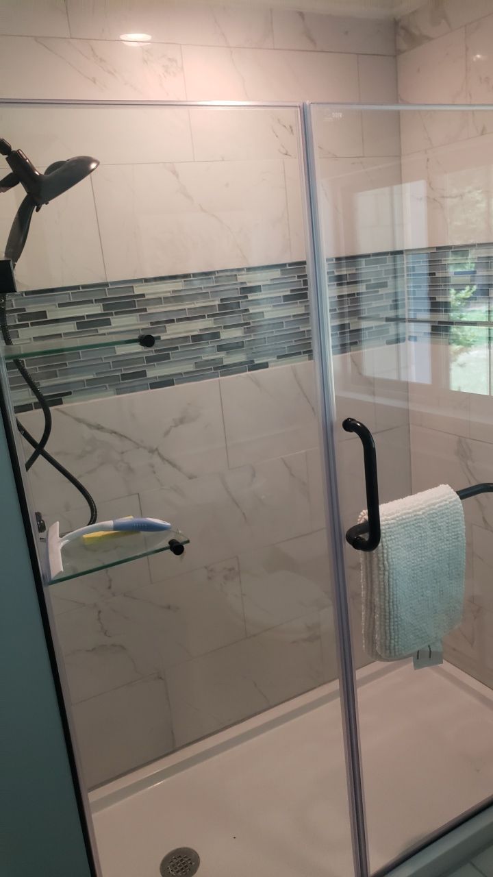 A bathroom with a walk in shower with a glass door and a towel rack.