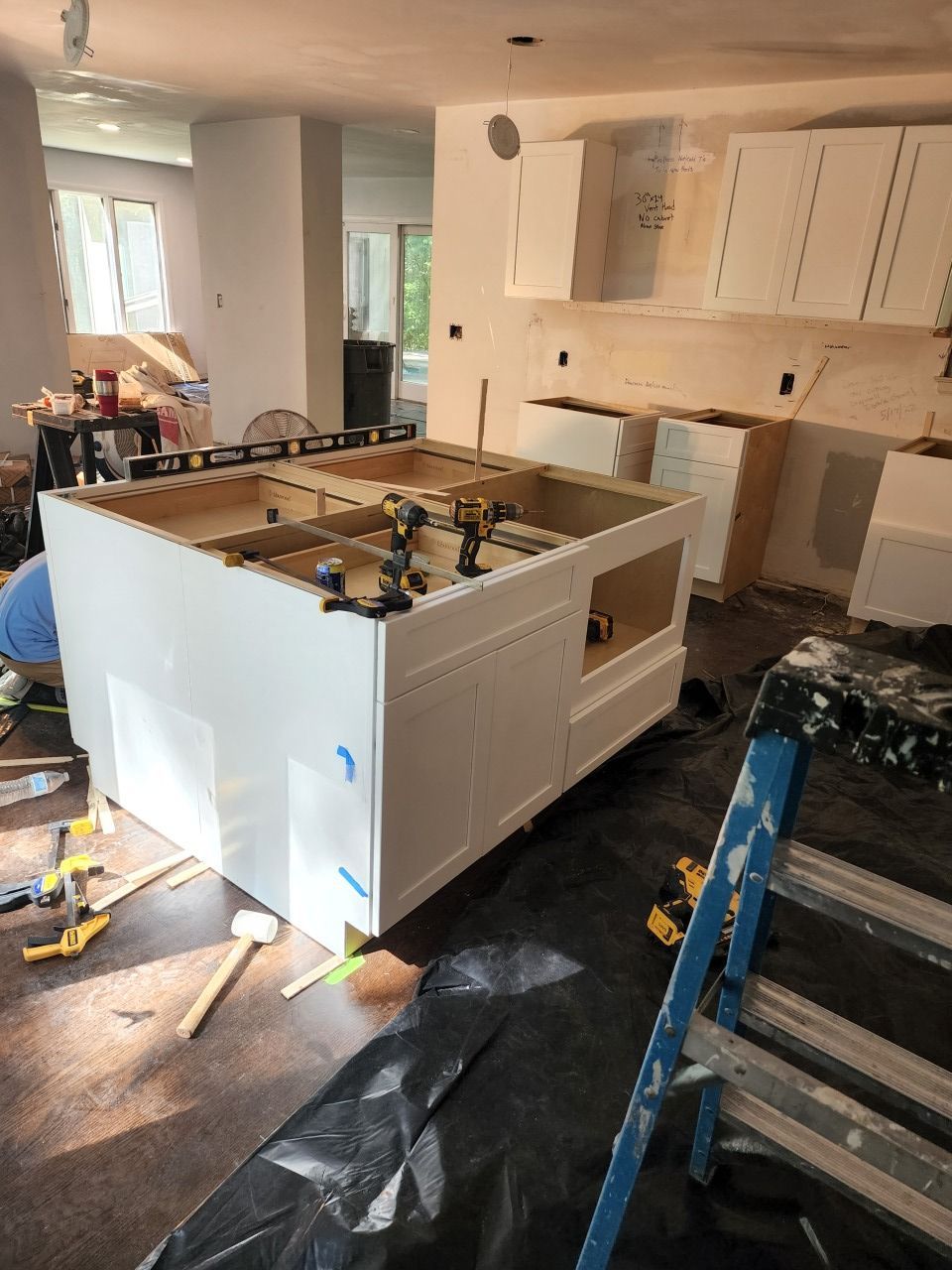 A kitchen is being remodeled with white cabinets and a blue ladder.