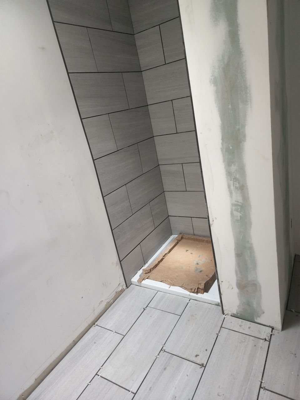 A corner of a bathroom with tiles on the floor and walls.