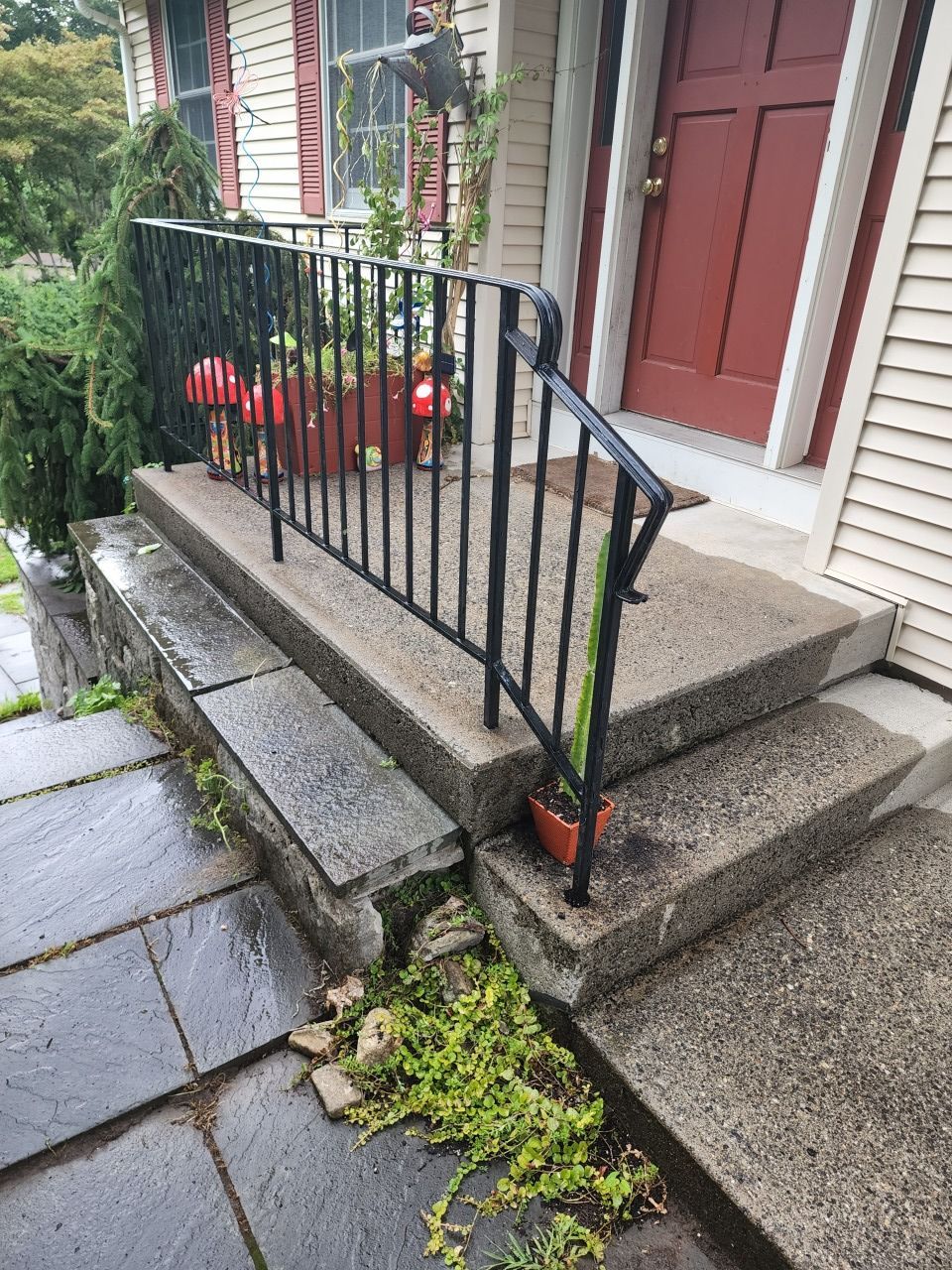 A concrete porch with a metal railing and steps leading to a red door.