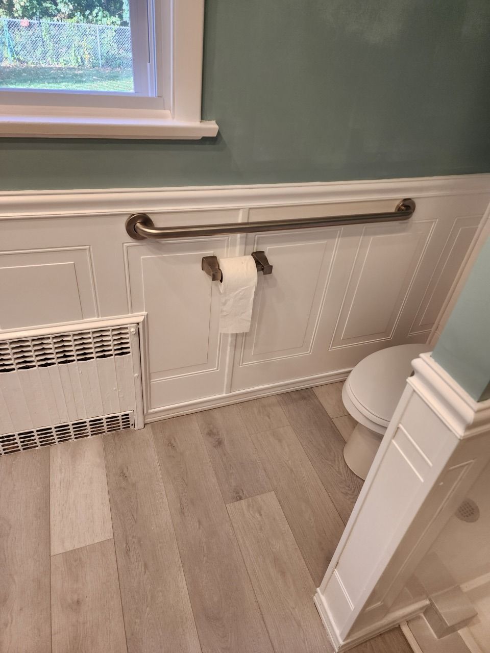 A bathroom with a toilet , a towel rack , and a window.