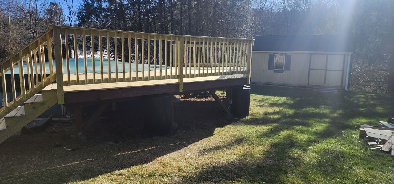 A wooden deck is sitting in front of a house next to a pool.