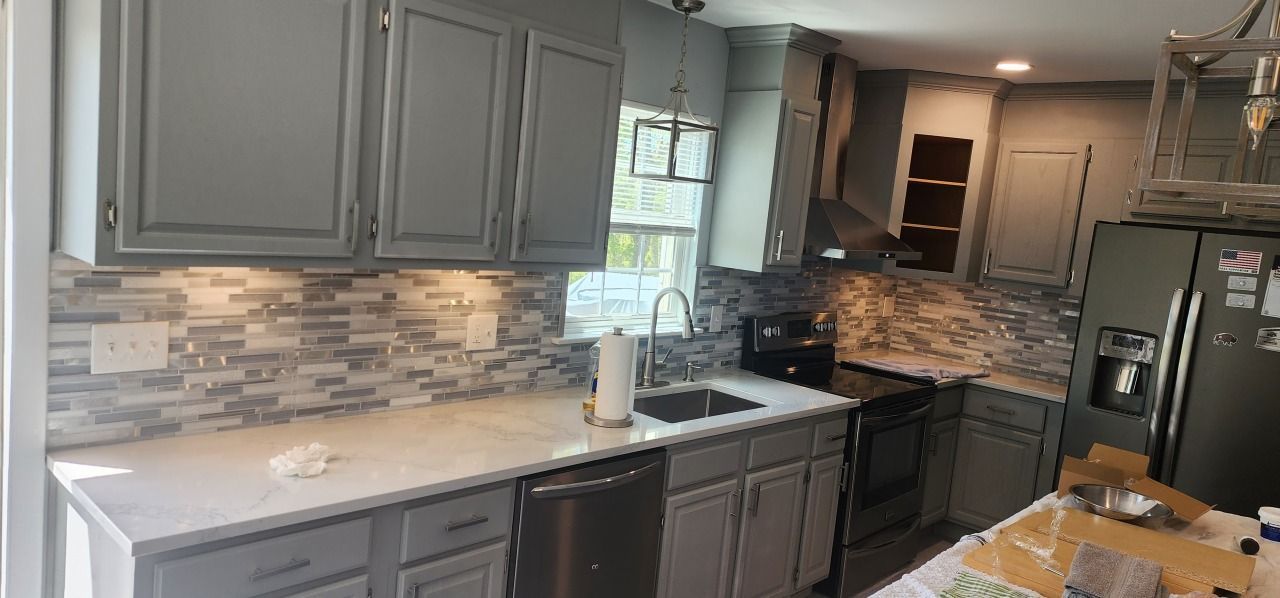 A kitchen with gray cabinets , white counter tops , stainless steel appliances , and a black refrigerator.