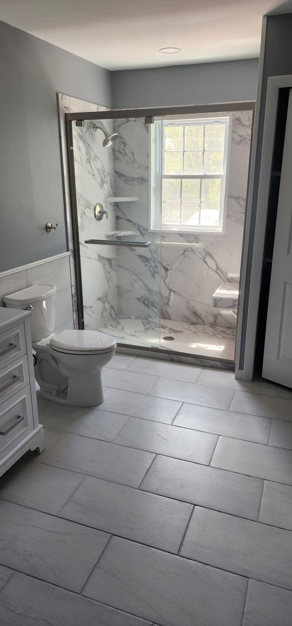 A bathroom with a toilet , sink , shower and window.