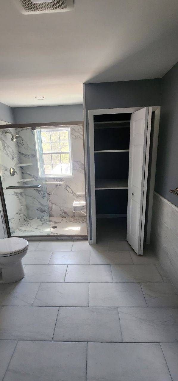 A bathroom with a toilet , shower , and closet.