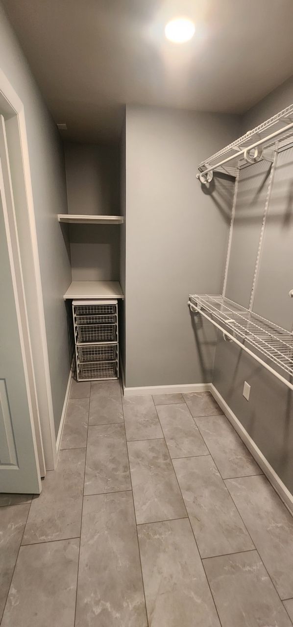 A walk in closet with a tiled floor and a shelf.