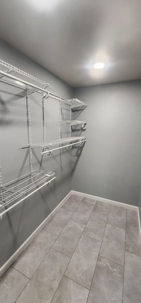 A walk in closet with lots of shelves and tile floors.