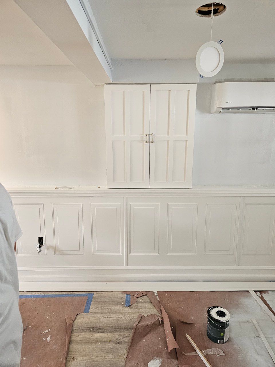 A person is standing in a room with white cabinets and a ceiling fan.
